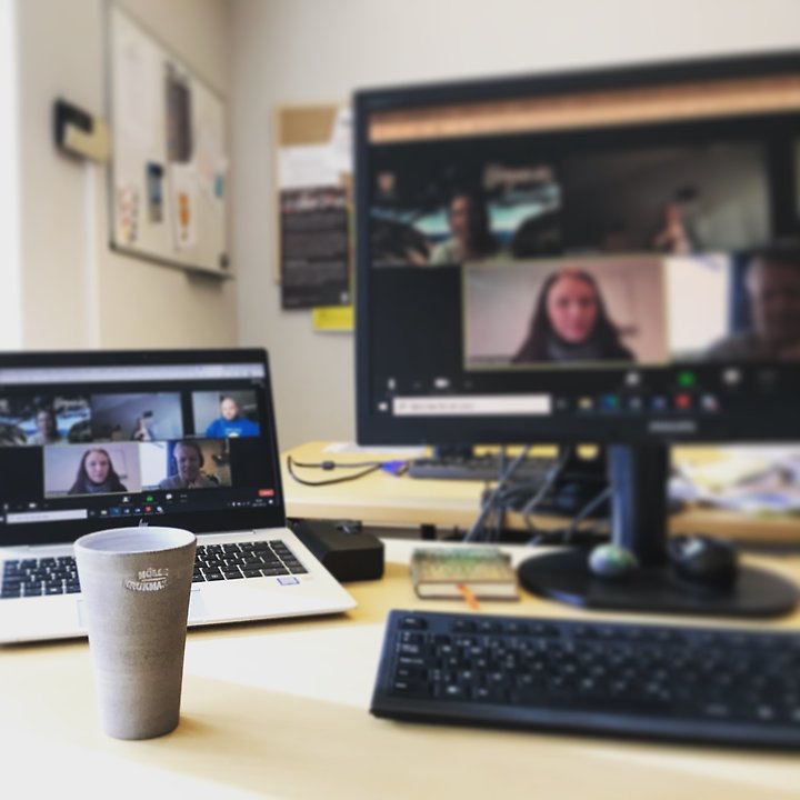 På bilden syns flera personer på två skärmar i ett digitalt möte. I förgrunden en kaffekopp. 