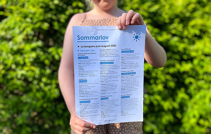 En flicka håller upp ett utskrivet blad från sommarlovsprogrammet. Foto.