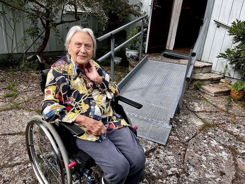 Äldre kvinna i rullstol utanför sin bostad